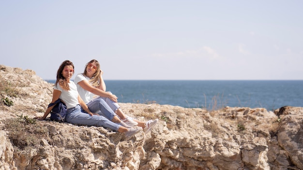 Amigos de largo alcance sentados en las rocas junto al océano con espacio de copia