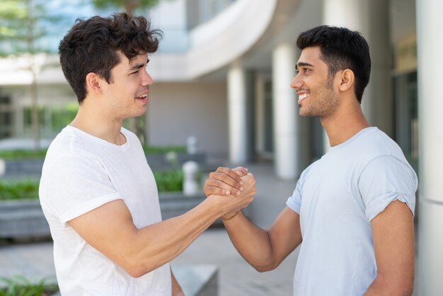 Amigos masculinos jovenes alegres que se encuentran y que saludan con el apretón de manos