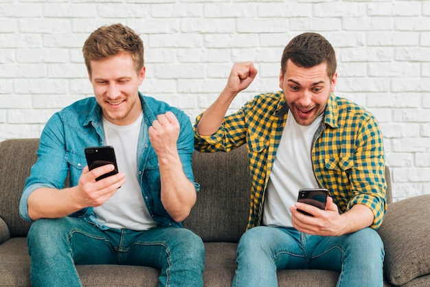 Foto gratuita amigos masculinos jovenes sonrientes que miran el teléfono elegante que aprieta su puño