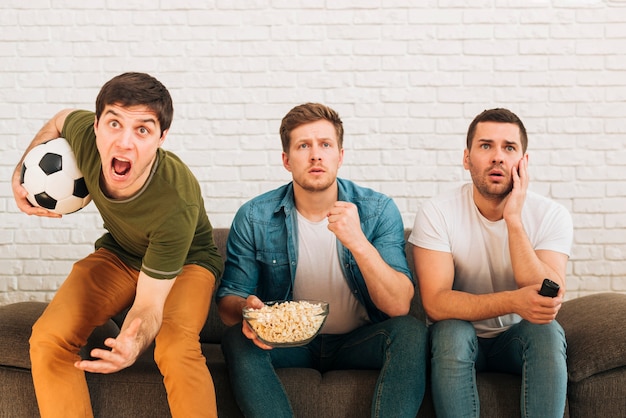 Amigos masculinos preocupados que se sientan en el sofá que mira el partido de fútbol en la televisión