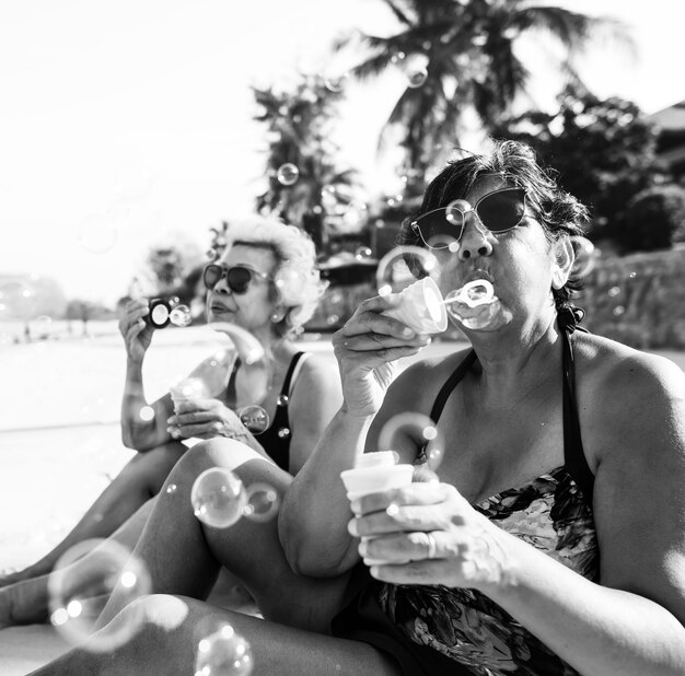 Amigos mayores que soplan burbujas y refrigeración en la playa
