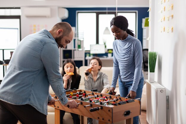 Amigos multiétnicos disfrutan del juego de futbolín después del trabajo