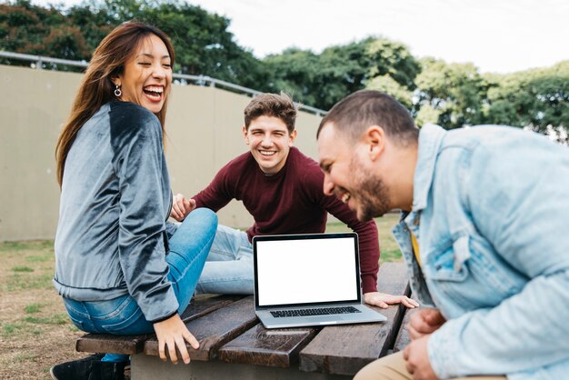 Amigos multiétnicos se divierten en el parque con laptop