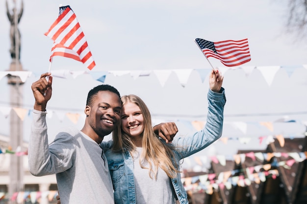 Amigos multiétnicos que sostienen banderas americanas en manos extendidas