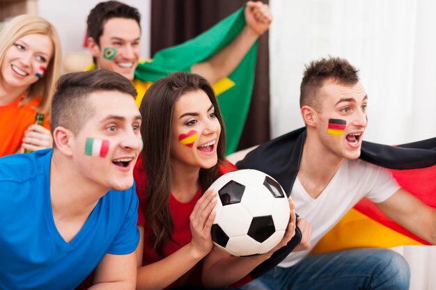 Amigos multinacionales animando el partido de fútbol en casa