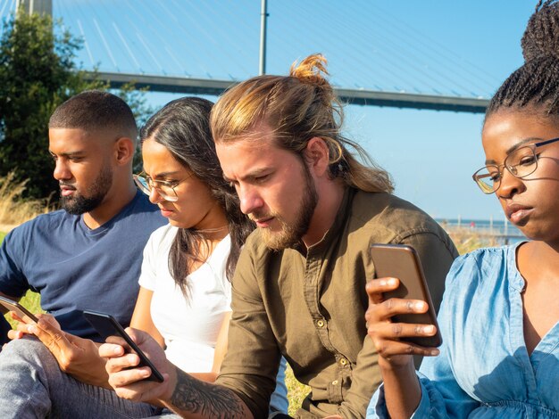 Amigos multirraciales enfocados que usan teléfonos inteligentes