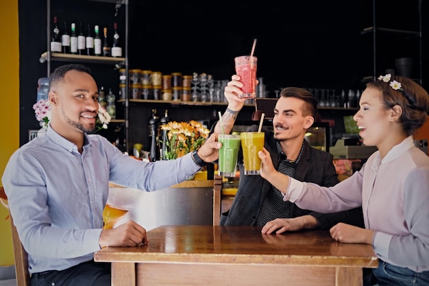 Amigos negros americanos y caucásicos beben cócteles veganos refrescantes en un restaurante.