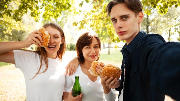 Amigos en el parque tomando selfie mientras come hamburguesas y cerveza