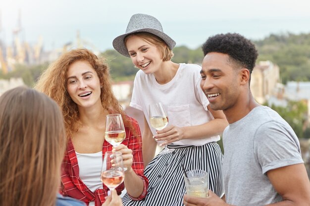 Amigos de pie en el balcón admirando los paisajes de la ciudad mientras beben cócteles