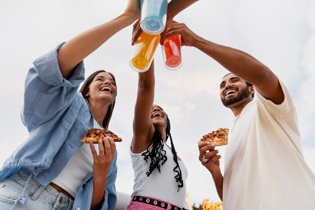 Amigos con pizza y bebidas de ángulo bajo.