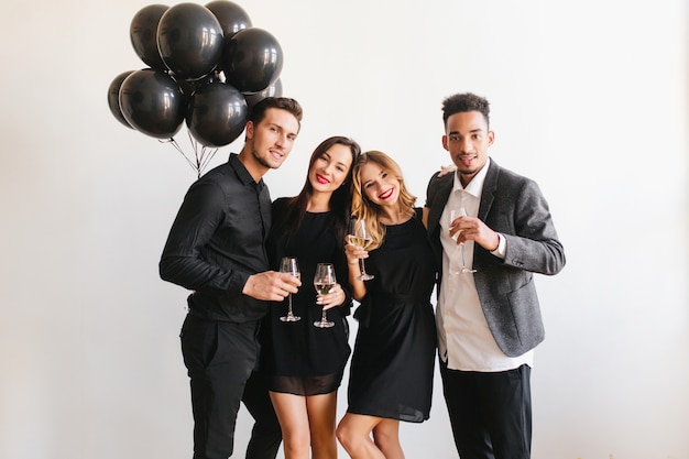 Amigos posando en la fiesta con copas de champán y globos negros