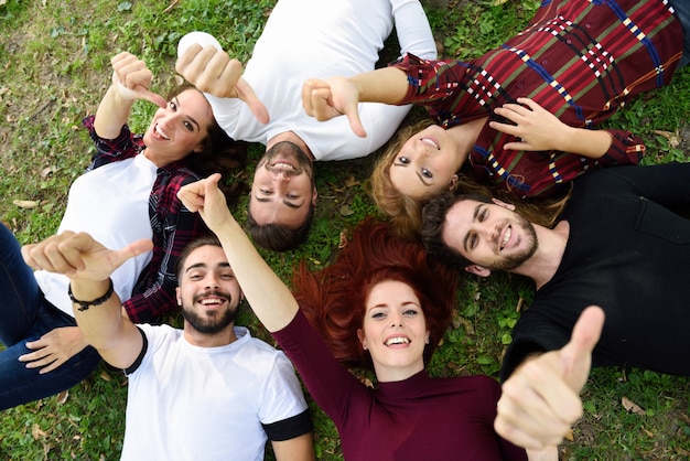 Amigos con los pulgares arriba y sonriendo, tumbados en el césped