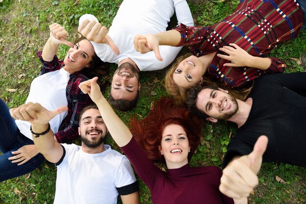 Amigos con los pulgares arriba y sonriendo, tumbados en el césped