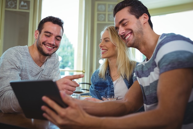 Amigos que se sientan a la mesa y que usa la tableta digital en cafetería ©