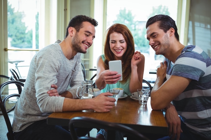 Foto gratuito amigos que se sientan a la mesa y usar el teléfono móvil en cafetería ©
