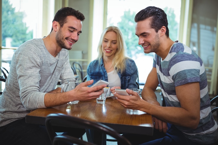 Foto gratuito amigos que se sientan a la mesa y usar el teléfono móvil en cafetería ©