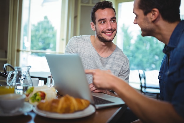 Amigos que se sientan a la mesa y utilizando equipo portátil en cafetería ©