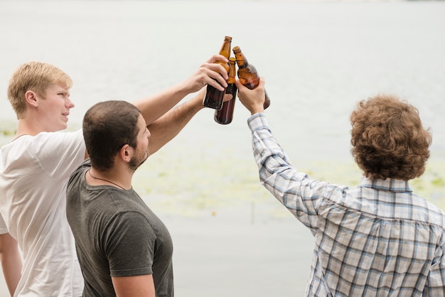 Foto gratuita amigos que tintinean botellas cerca del agua