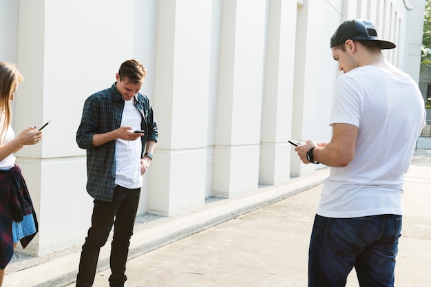 Amigos que usan teléfonos inteligentes juntos al aire libre y refrigeración