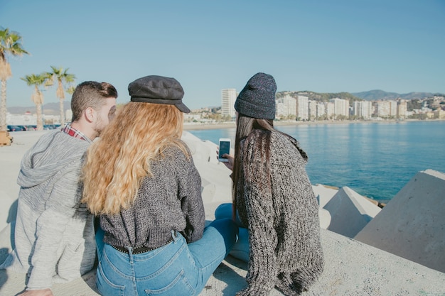 Amigos sentados al lado del mar con smartphone