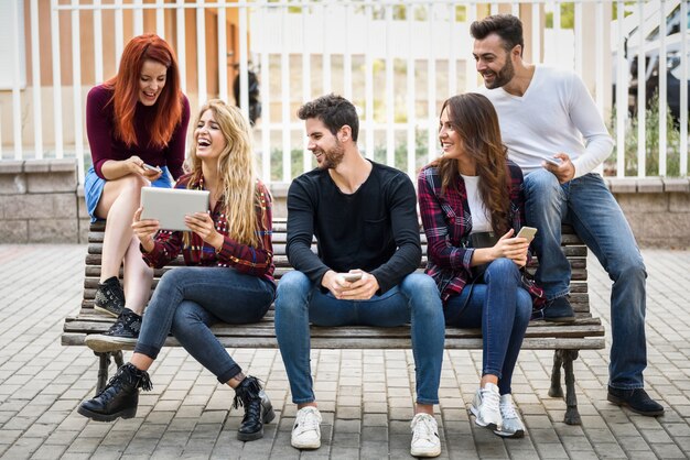 Amigos sentados en un banco de madera en la calle y mirando una tablet de una chica