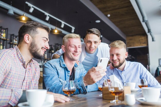 Amigos sentados en el bar con bebidas mirando el teléfono móvil