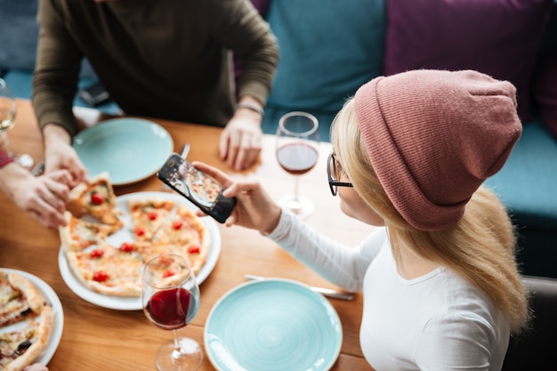 Amigos sentados en la cafetería hacen una foto de pizza