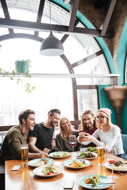 Foto gratuita amigos sentados en la cafetería y usando el teléfono móvil.