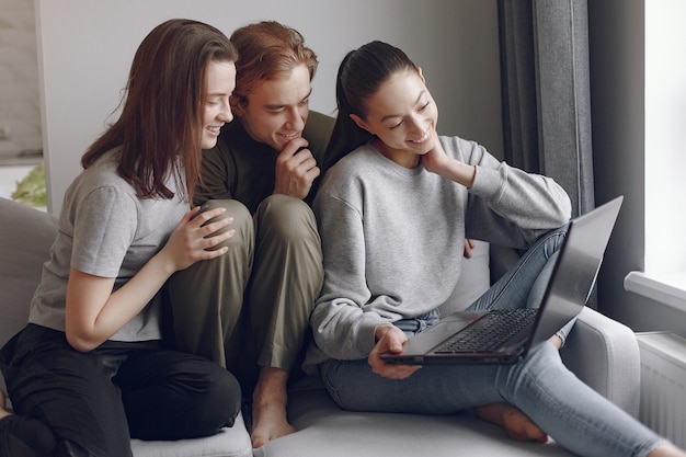 Amigos sentados en una cama en una habitación y usan una computadora portátil