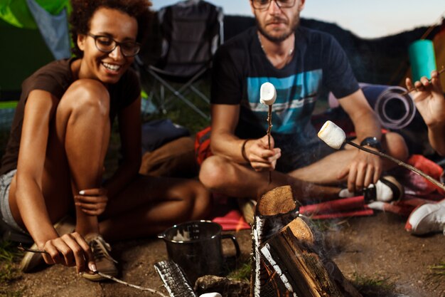 Amigos sentados cerca de la hoguera, sonriendo, tocando la guitarra