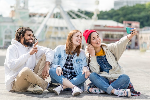 Foto gratuita amigos sentados en el piso y tomando selfie