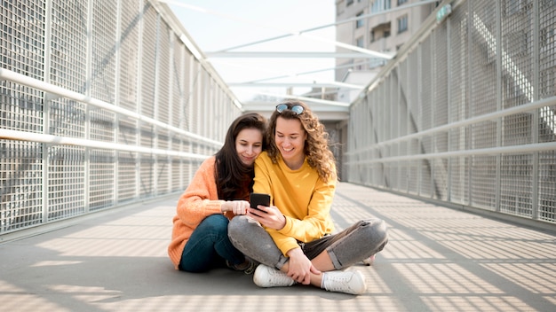 Amigos sentados en un puente y mirando su teléfono