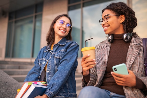 Foto gratuita amigos sonrientes con libros tomando café juntos al aire libre