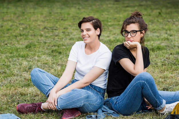 Amigos sonrientes de las muchachas que se sientan en hierba del parque