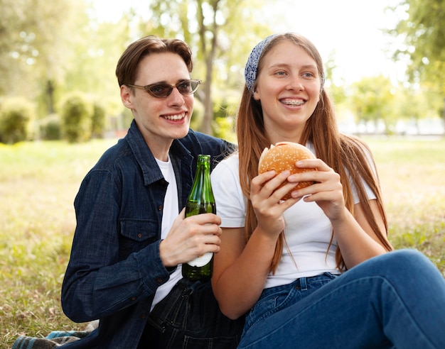 Amigos sonrientes en el parque con cerveza y hamburguesa