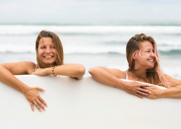 Foto gratuita amigos sonrientes en la playa con tabla de surf