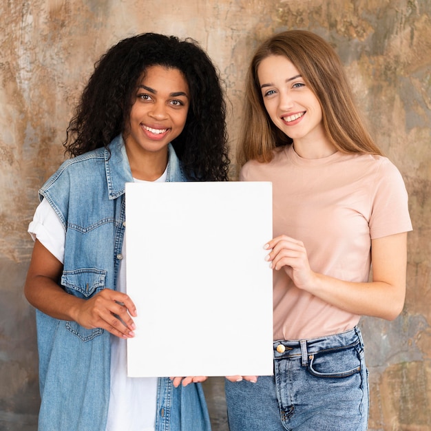 Foto gratuita amigos sonrientes posando juntos y sosteniendo un cartel en blanco