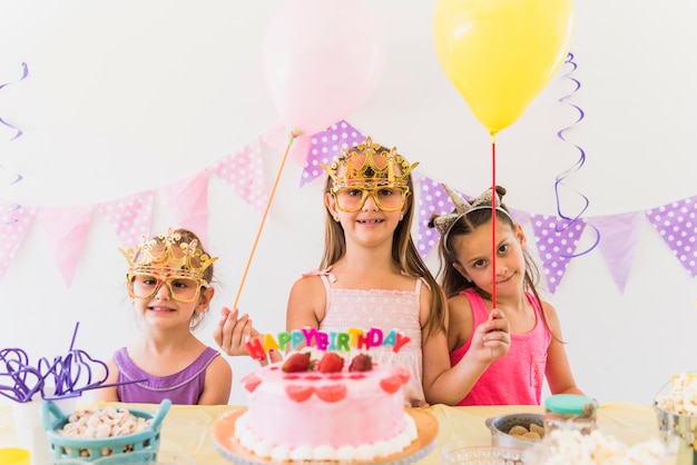 Amigos sonrientes que llevan la máscara de ojo que sostiene los globos que gozan en fiesta de cumpleaños