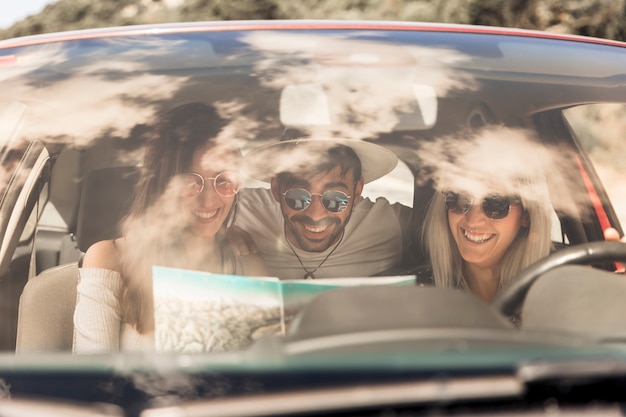 Amigos sonrientes que miran el mapa que se sienta dentro del coche