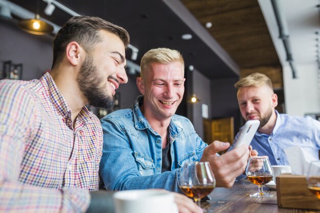 Amigos sonrientes que se sientan en la barra que mira el teléfono móvil