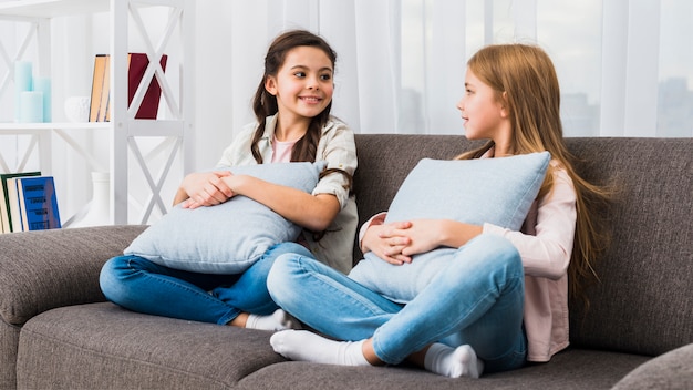 Amigos sonrientes que se sientan en el sofá con el amortiguador que mira el uno al otro