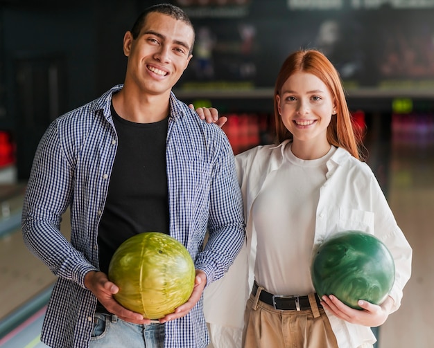 Amigos sonrientes que sostienen las bolas de bolos coloridas tiro medio