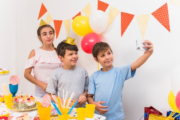 Amigos sonrientes que toman selfie en el teléfono móvil mientras celebran la fiesta de cumpleaños