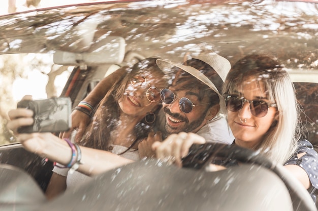 Amigos sonrientes que viajan en coche tomando selfie a través del móvil