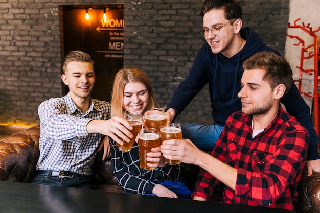 Amigos sonrientes sentados juntos tostando los vasos de cerveza