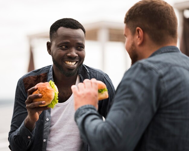 Amigos sonrientes de tiro medio sosteniendo hamburguesas