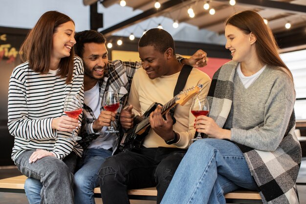 Amigos sosteniendo bebidas mientras escuchan a su amigo tocando la guitarra