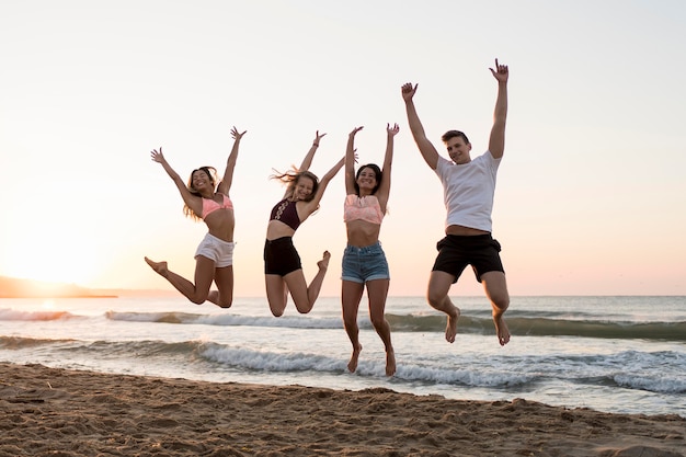 Foto gratuita amigos de tiro completo saltando en la playa