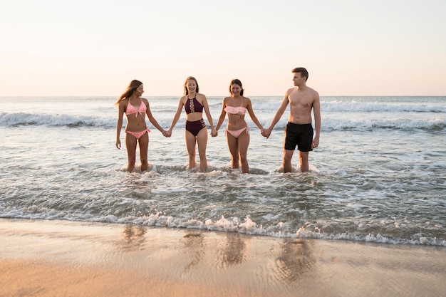 Amigos de tiro completo tomados de la mano en la playa