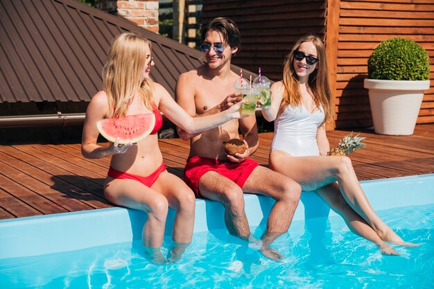 Amigos de tiro largo disfrutando de cócteles en la piscina